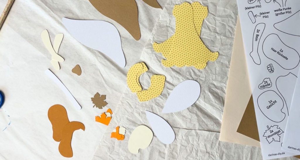 Ausgeschnittene Papierteile für eine Waldfee neben der gedruckten Bastelvorlage
