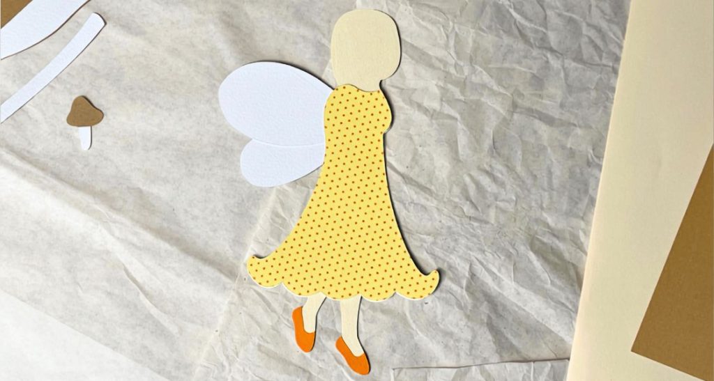 Teilweise zusammengesetzte Waldfee aus Papier mit gelbem Kleid, weißen Flügeln und orangefarbenen Schuhen